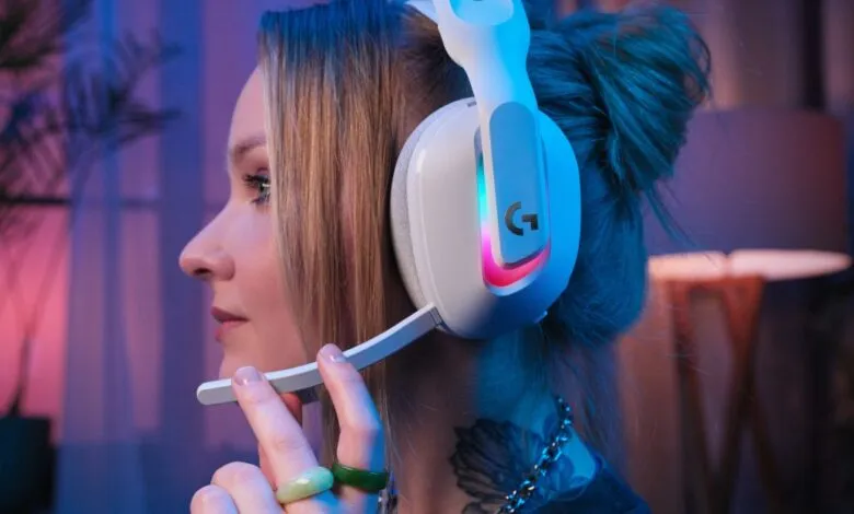 Woman wearing white Logitech G gaming headset with RGB lighting, adjusting the microphone.