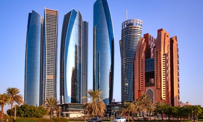 Modern skyscrapers in Abu Dhabi, UAE, reflecting sunlight. Palm trees and a car are in the foreground.