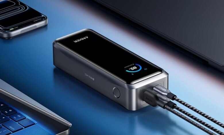 Anker power bank charging a laptop, smartphone, and tablet on a blue surface.