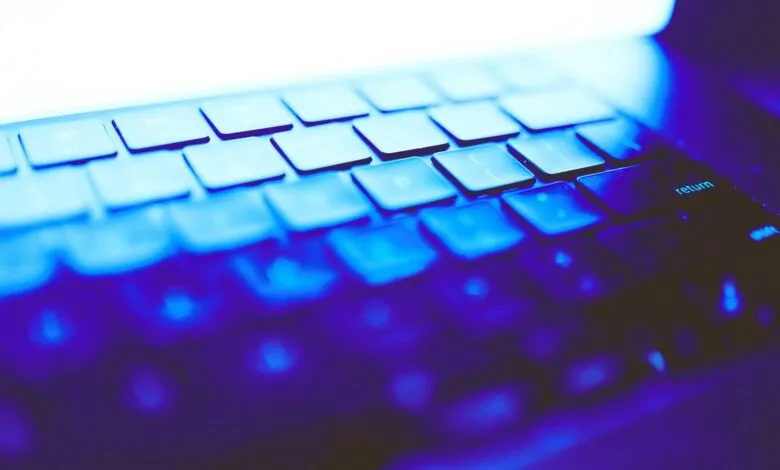 Close-up of a laptop keyboard illuminated in blue light, focusing on the 'return' key.