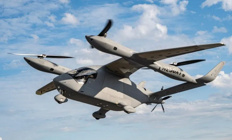 A gray electric vertical takeoff and landing (eVTOL) aircraft in flight against a partly cloudy blue sky.