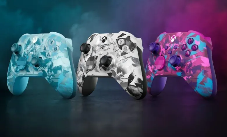 Three Xbox controllers in teal, gray, and purple with abstract designs.