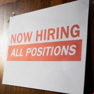 A white sign with red text reads 'NOW HIRING ALL POSITIONS'.