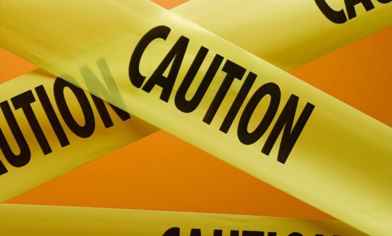 Close-up of yellow caution tape crisscrossed against an orange background. The word CAUTION is prominently displayed.