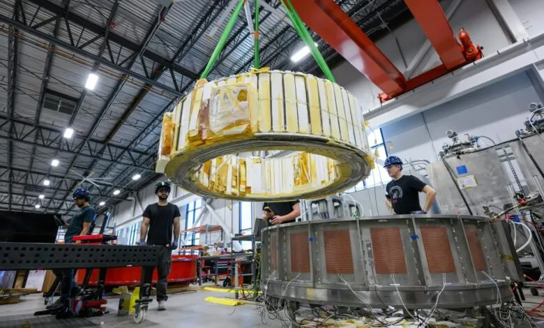 Scientists assemble a large, ring-shaped component in a high-tech lab, using a crane for precision.