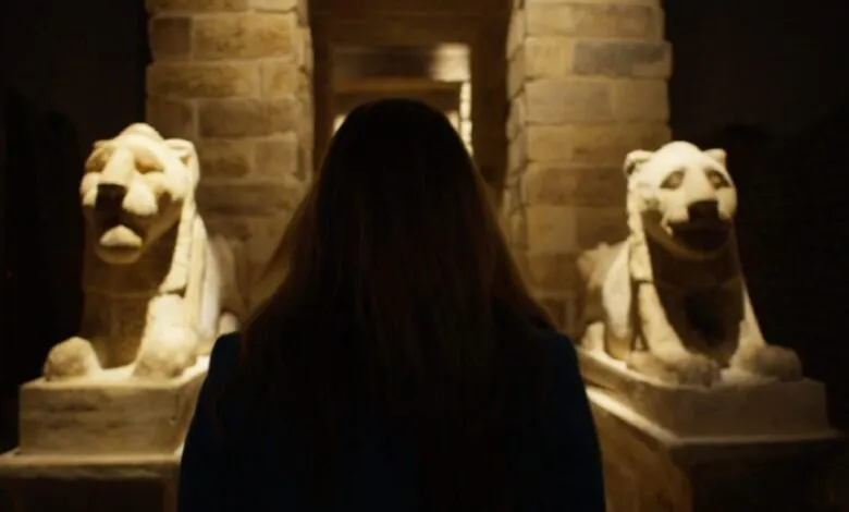 Woman stands between two ancient stone lion statues in a dimly lit museum or historical site.