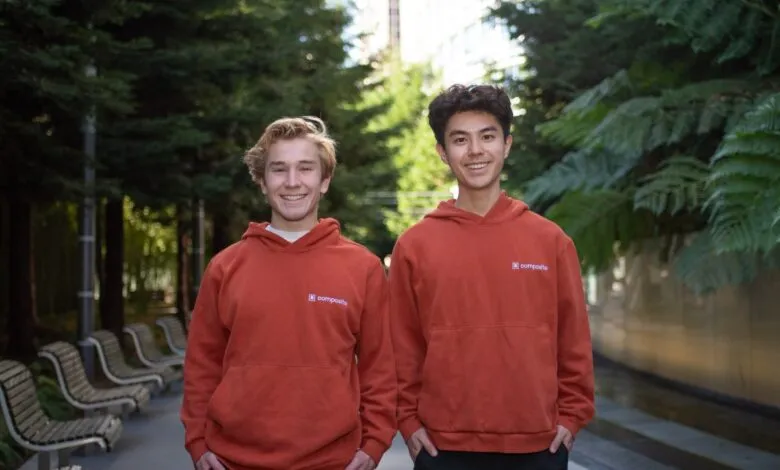 Two young men in matching orange hoodies with a company logo stand outdoors.