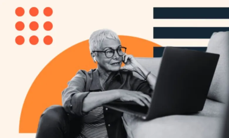 Elderly woman with short white hair and glasses using a laptop on a couch.
