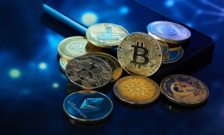 Various cryptocurrencies like Bitcoin, Ethereum, and Dogecoin rest on a smartphone. Gold and dark-colored coins reflect on a dark surface.