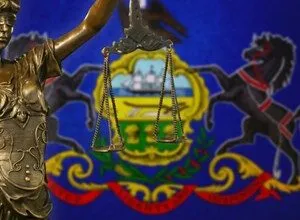 Statue of Justice holding scales in front of Pennsylvania state flag.