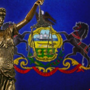 Statue of Justice holding scales in front of Pennsylvania state flag.
