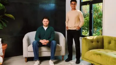 Two men, one seated and one standing, pose for a portrait in a modern, well-lit room.