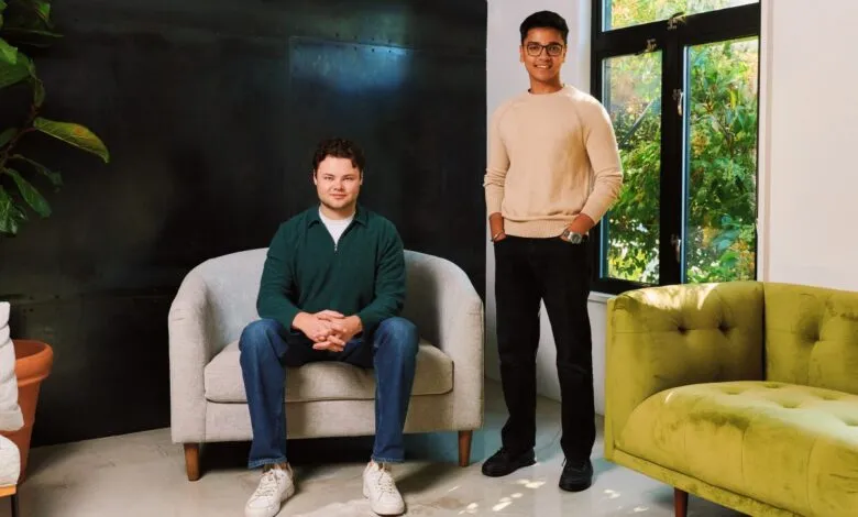 Two men, one seated and one standing, pose for a portrait in a modern, well-lit room.