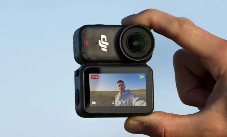 Person holding a DJI Osmo Action 3 camera, recording a selfie video outdoors.