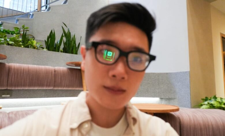 Person wearing glasses with a green digital overlay showing in the lenses, sitting in a modern lobby.