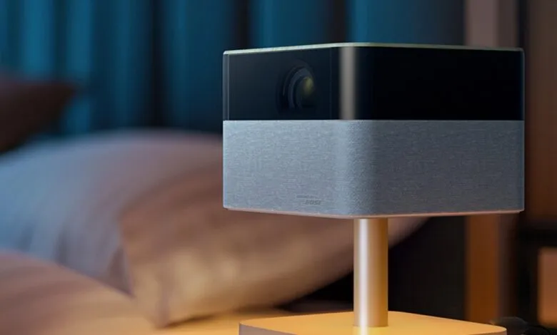 Compact Epson projector with Bose sound, sitting on a bedside table in a dimly lit room.