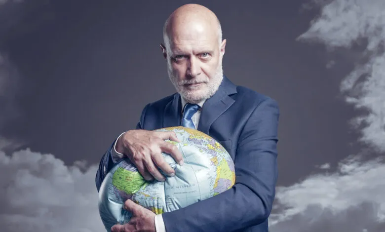 A businessman in a suit holds a deflated globe, conveying global challenges.