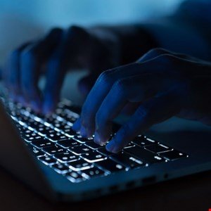 Close-up of hands typing on a laptop keyboard in low light.