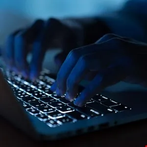 Close-up of hands typing on a laptop keyboard in low light.