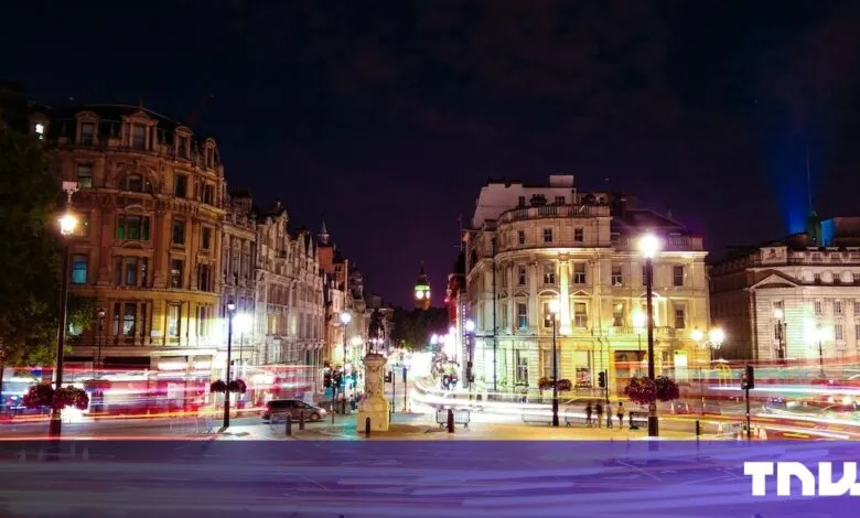Night view of London street with Big Ben in distance, light trails from traffic, and classic architecture.