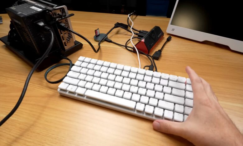 A compact white keyboard is connected to a small computer setup with a monitor and graphics card.