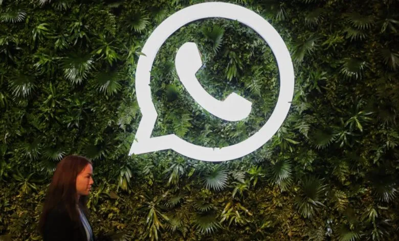 WhatsApp logo illuminated on a lush green wall, a woman walks past.