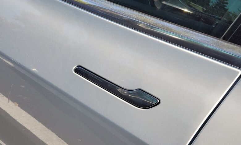 Close-up of a sleek, black Tesla door handle on a silver car.