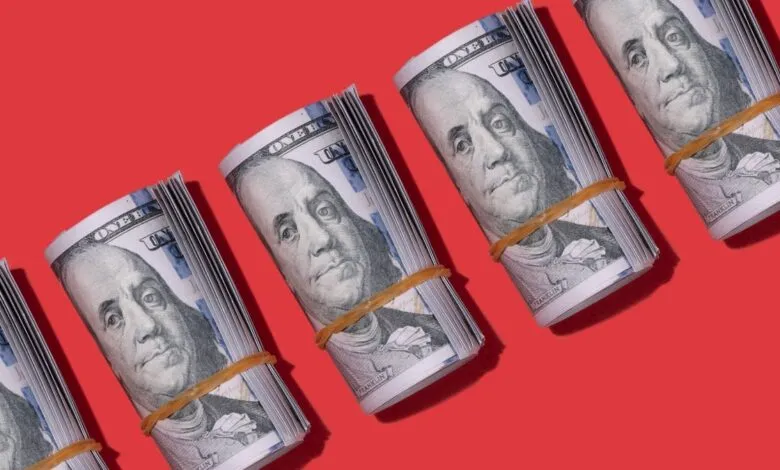 Bundles of US hundred dollar bills rolled and secured with rubber bands on a red background.