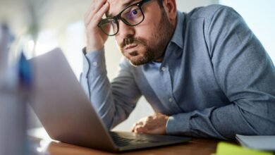 Frustrated businessman looking at laptop screen, hand on forehead.