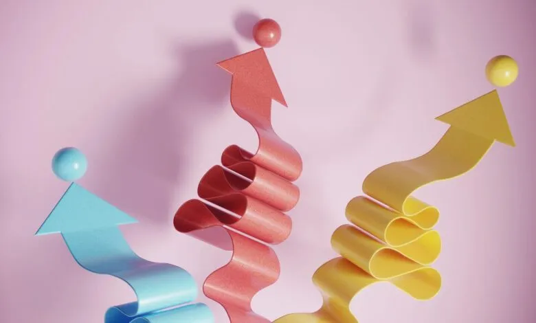 Three colorful upward arrows, each with a sphere on top, against a pink background. Represents growth or progress.