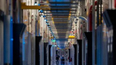 Two technicians walk down a long corridor in a data center; rows of servers line the walls, illuminated by blue lights.