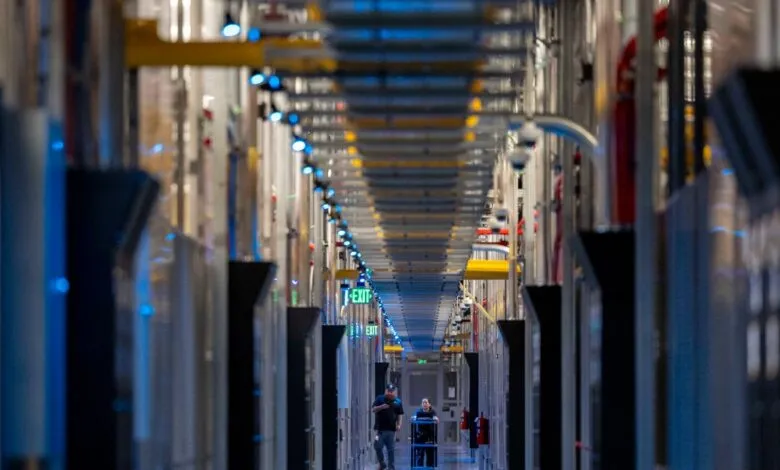 Two technicians walk down a long corridor in a data center; rows of servers line the walls, illuminated by blue lights.