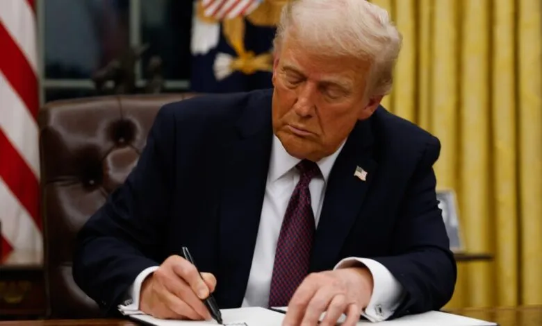 Donald Trump, former US President, sits at a desk in the Oval Office, signing a document.