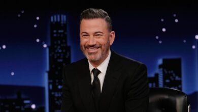 Jimmy Kimmel, smiling, in a black suit against a cityscape backdrop.