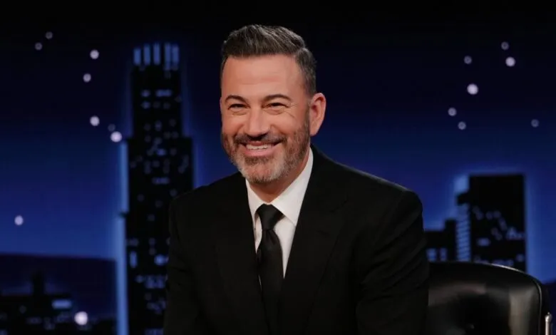 Jimmy Kimmel, smiling, in a black suit against a cityscape backdrop.