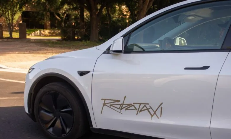 White Tesla Model Y with a RoboTaxi decal driving down a residential street.