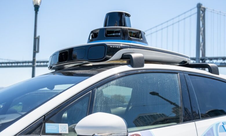 Waymo self-driving car with sensors on its roof, parked near a bridge.