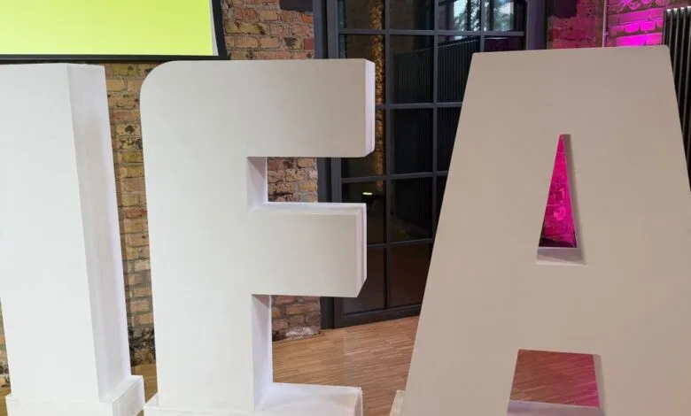 Large white letters spelling IFA stand in a brick room. Pink lighting accents the 'A'.
