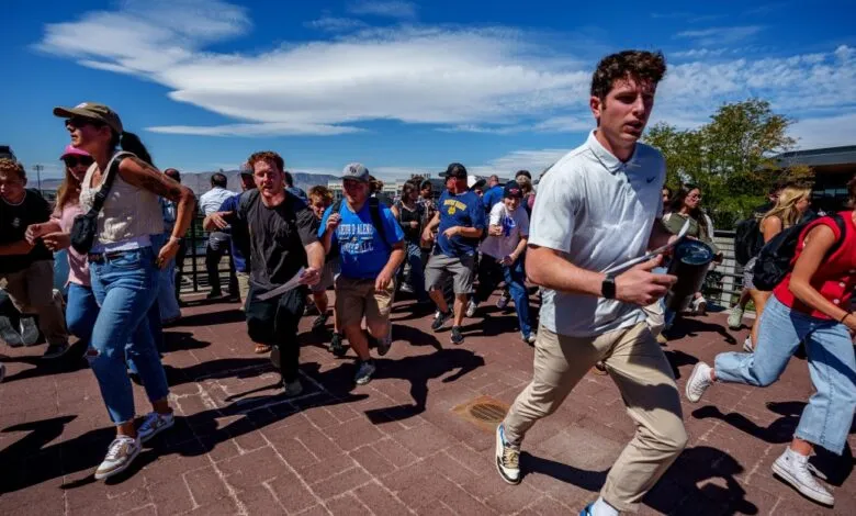A large group of people rush across a brick walkway, a sunny day in the background.