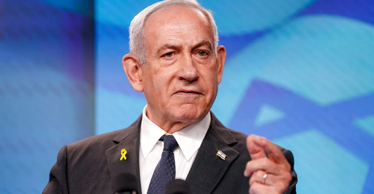 Benjamin Netanyahu, Israeli Prime Minister, speaks at a press conference, wearing a suit and a yellow ribbon.