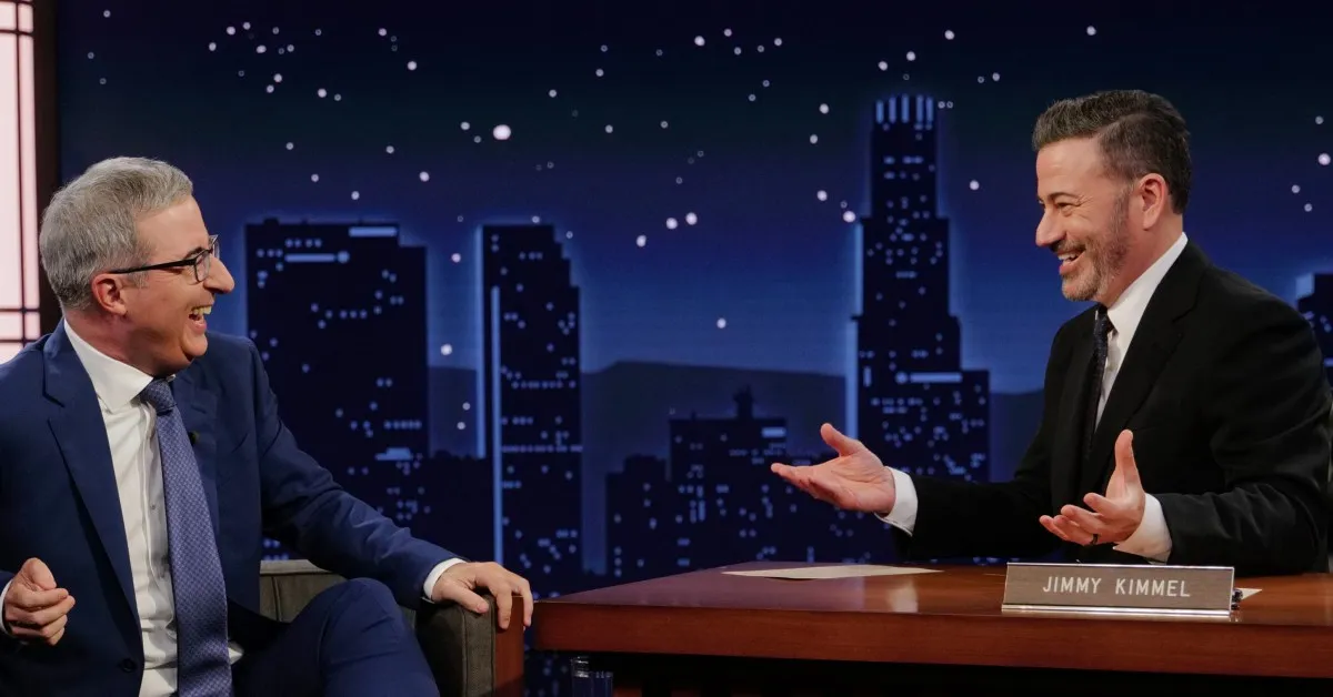 Stephen Colbert and Jimmy Kimmel laughing together on a talk show set.