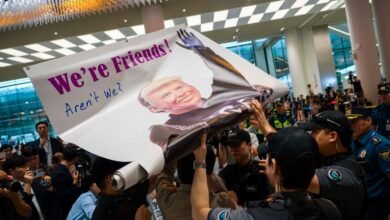 A banner with a caricature of Donald Trump and the text 'We're Friends! Aren't We?' is held up by people at an airport.