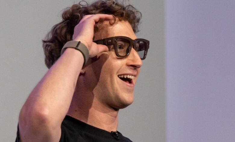 Smiling man with curly hair wearing glasses and a smartwatch, adjusting his glasses.