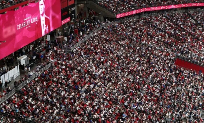 A large stadium crowd watches a memorial for Charlie Kirk displayed on a pink jumbotron.