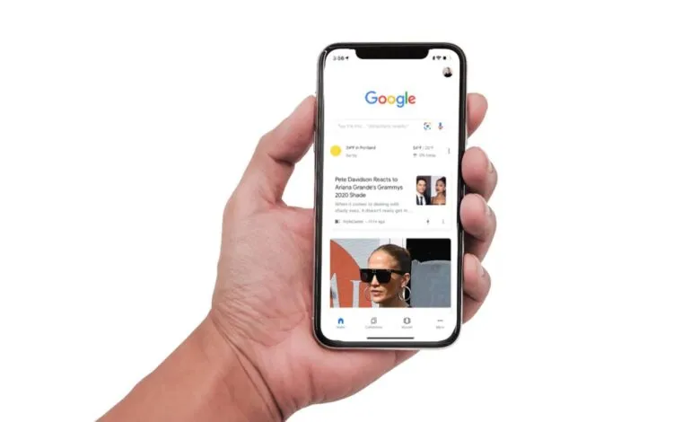 Hand holding smartphone displaying Google Discover feed with news articles about Pete Davidson and Ariana Grande, and Jennifer Lopez.