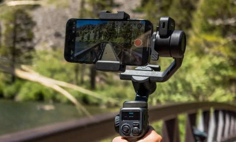 Smartphone mounted on a GoPro gimbal, recording video of a scenic bridge and lake.