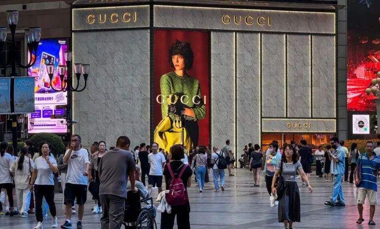 A large Gucci store in a busy city, featuring a model in a green sweater on a billboard.