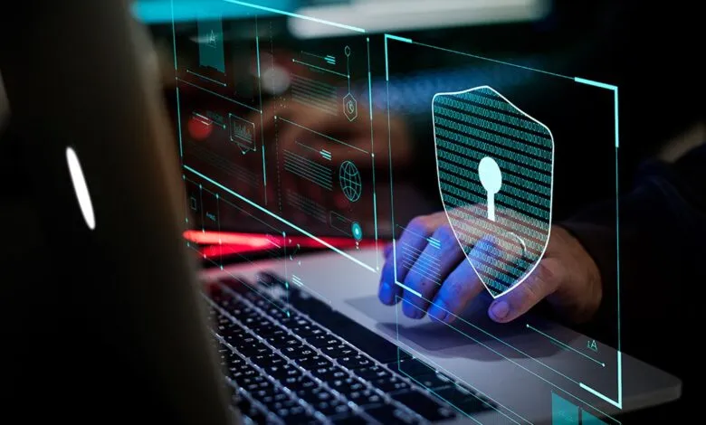 Person's hand interacts with a laptop screen displaying a digital shield and binary code, symbolizing cybersecurity.