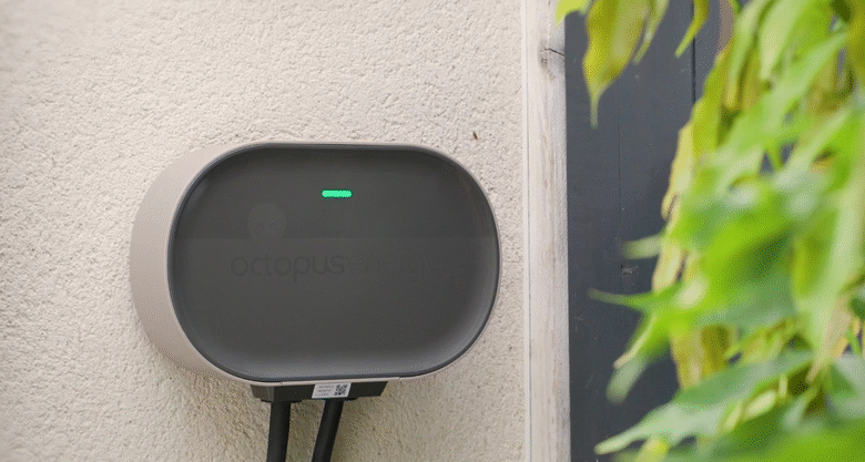 Octopus Energy electric vehicle charger mounted on a light beige wall, with a green indicator light.