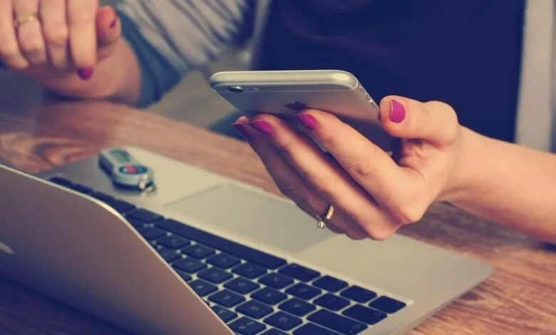Close-up of a woman's hands using a smartphone and laptop.